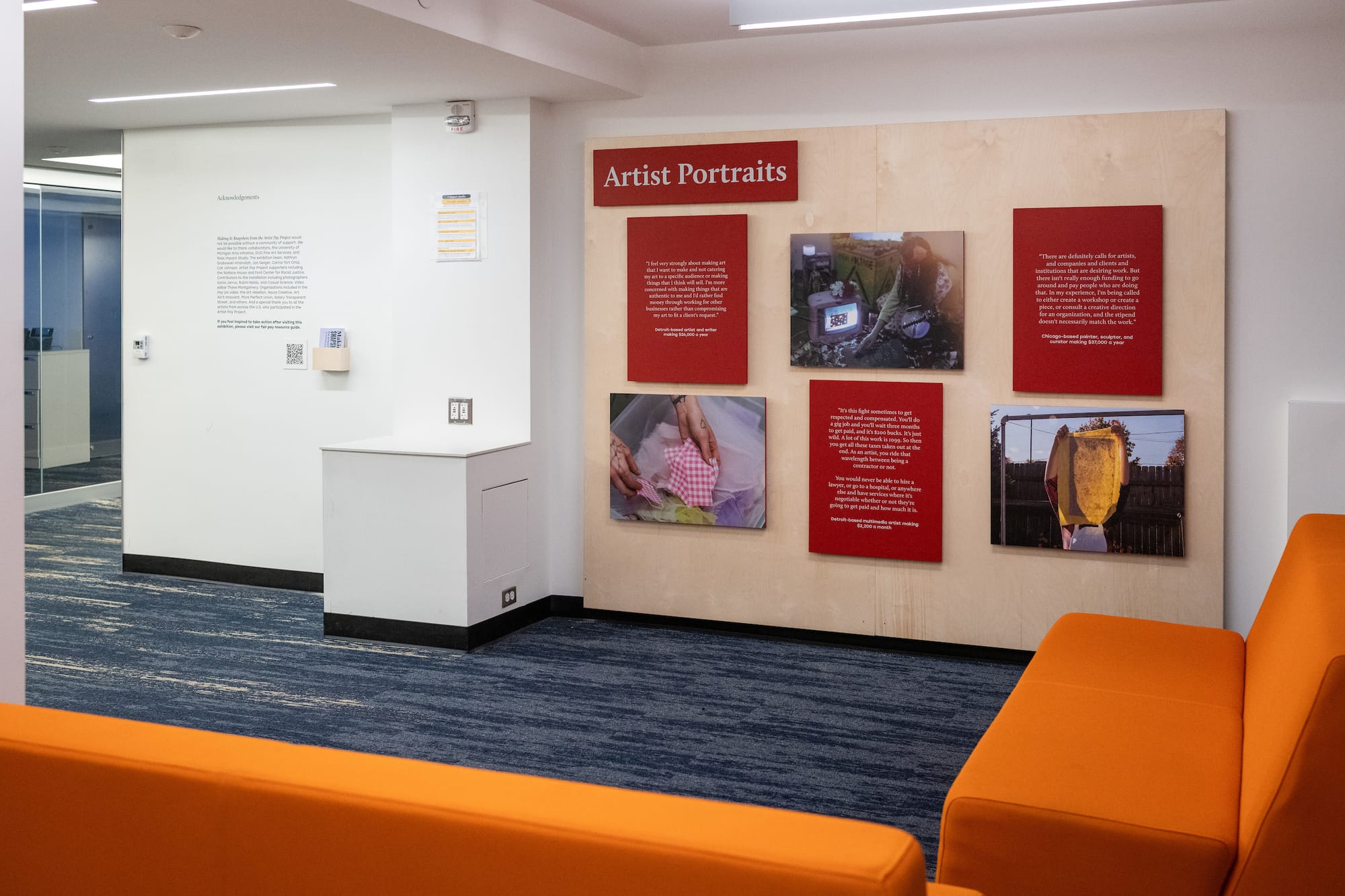 Behind orange couches is one of the installation sections focused on artist portraits. It features 6 red wood panels. Three are photos, the other 3 are quotes.