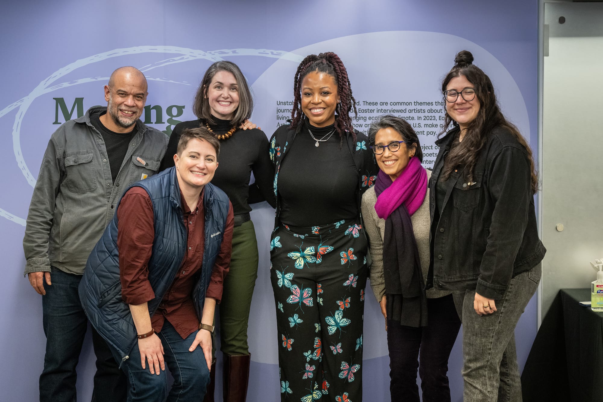 Six people stand smiling in front of the opening text of the installation