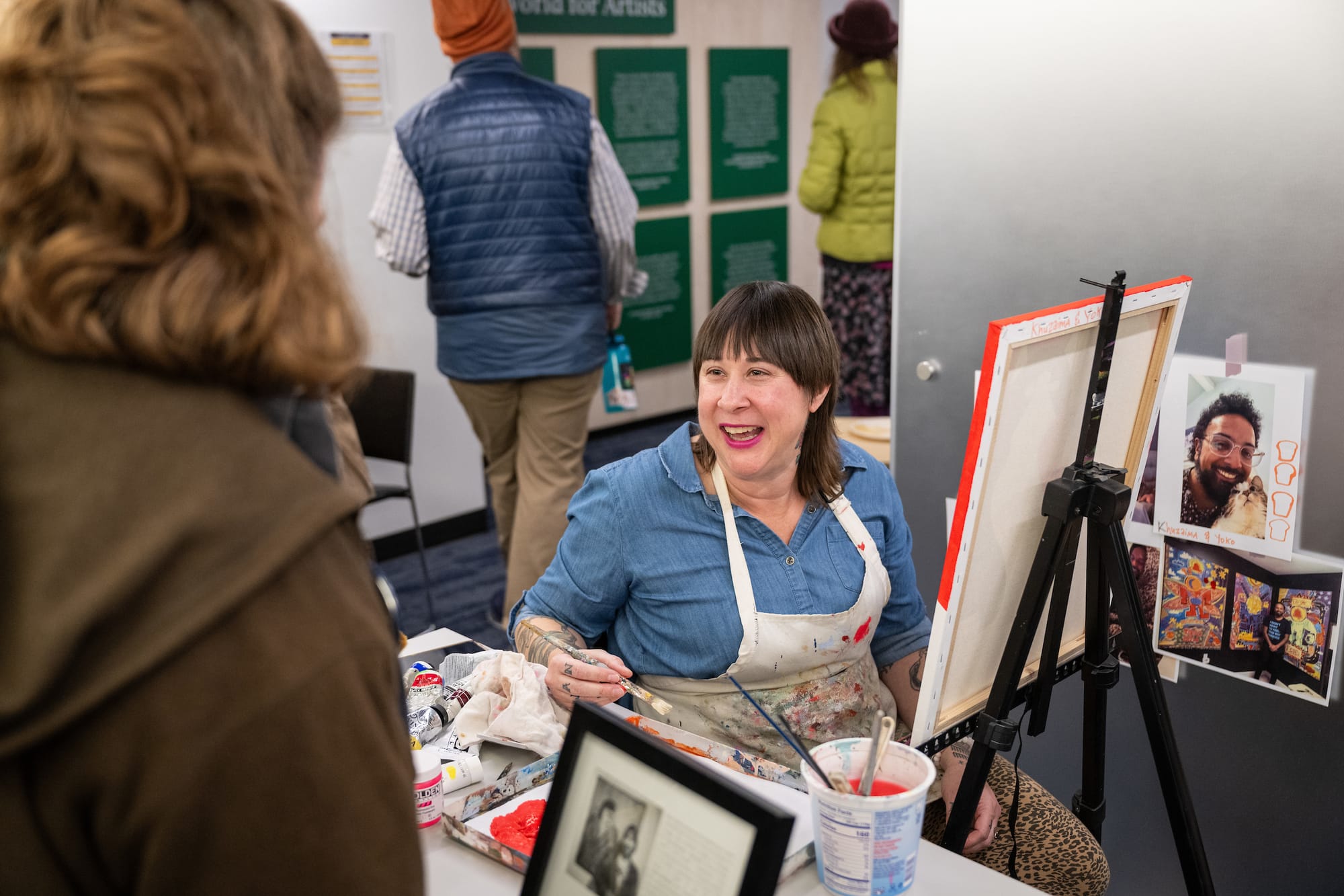 Photo of a painter smiling in a paint-splattered apron while working on a new commission