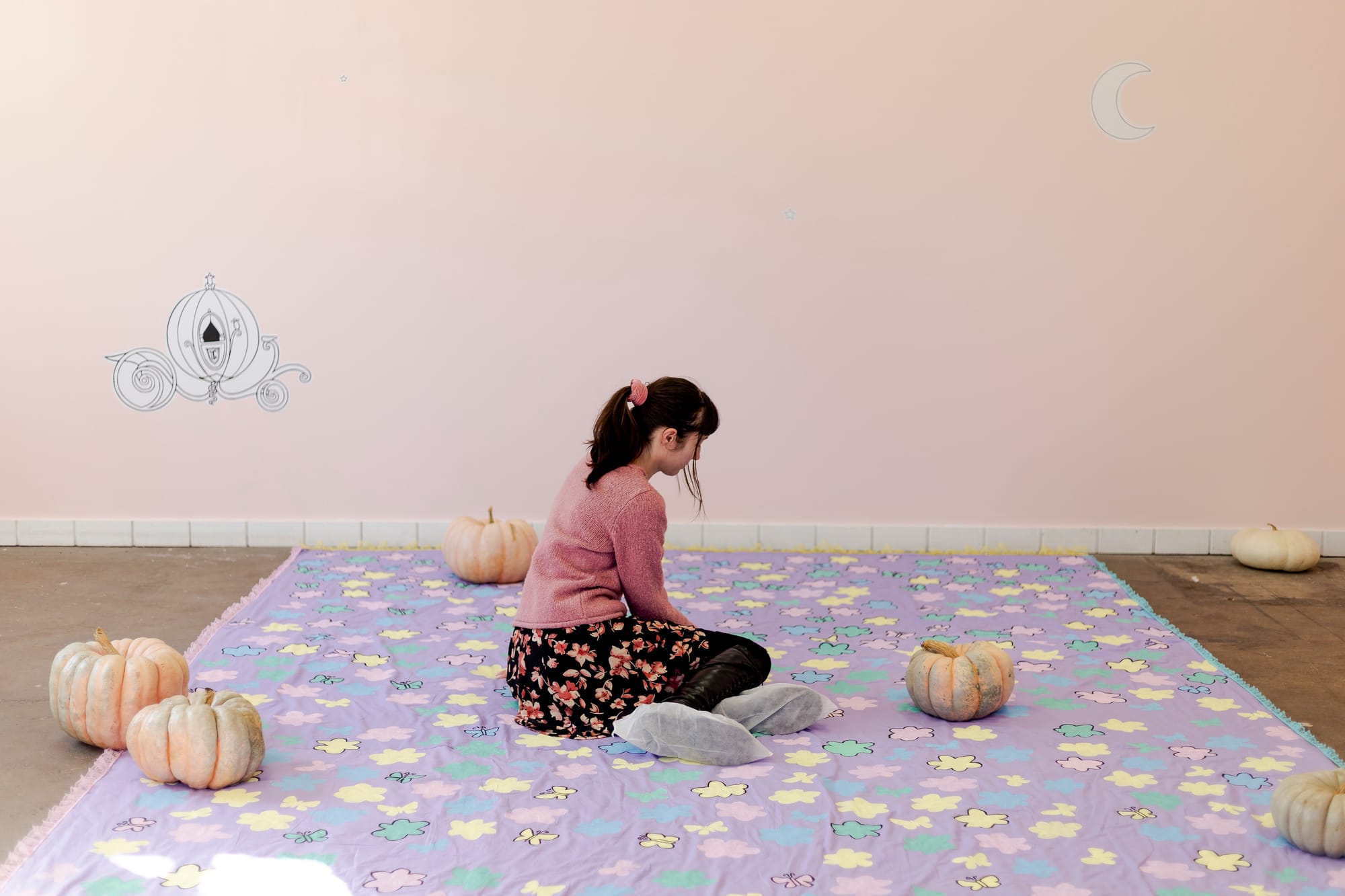 A woman with dark hair sits on a colorful quilt with light orange pumpkins. Her back is to the camera