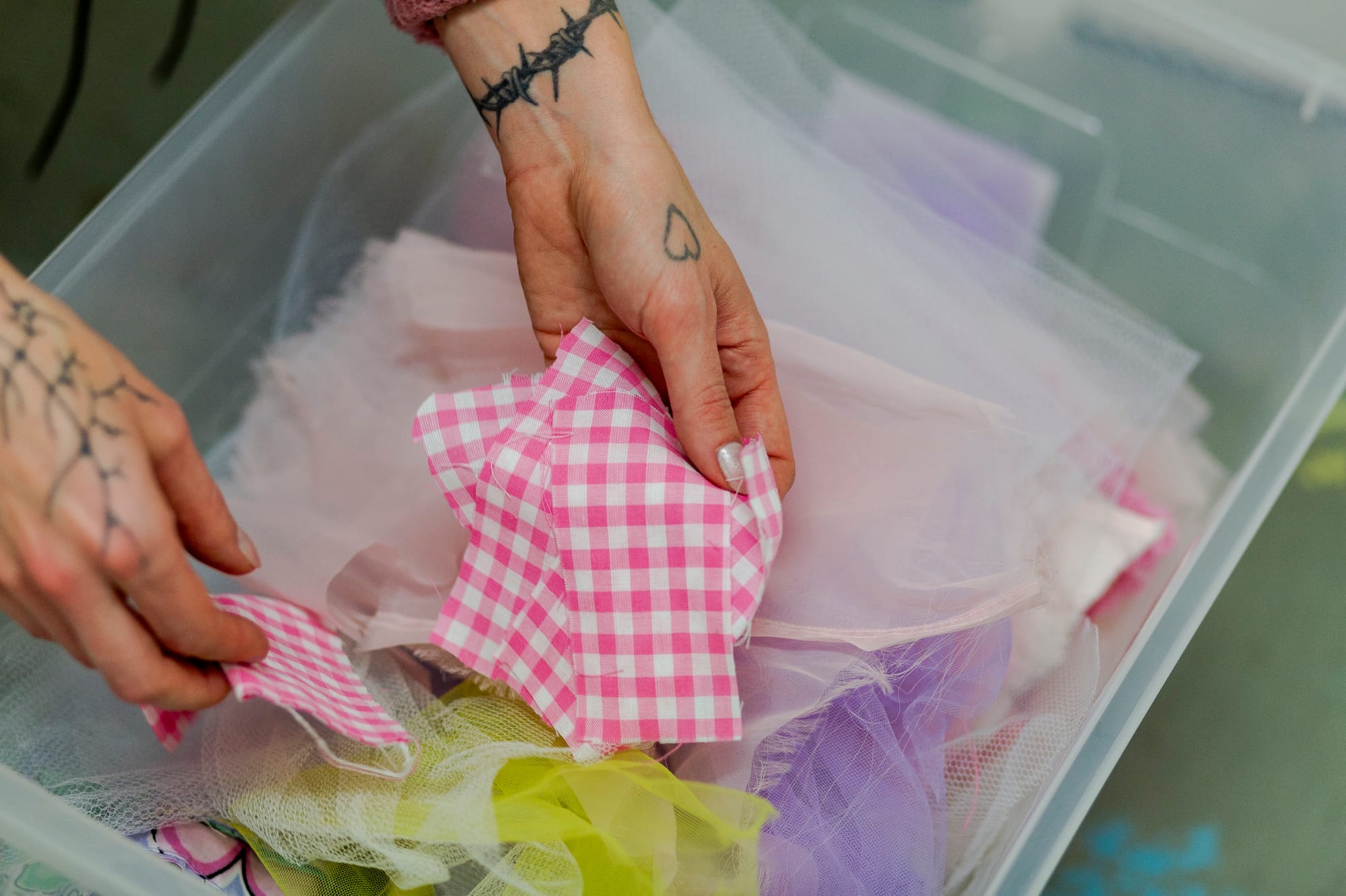 A close up image of tattooed hands holding pink and white gingham scraps of fabric