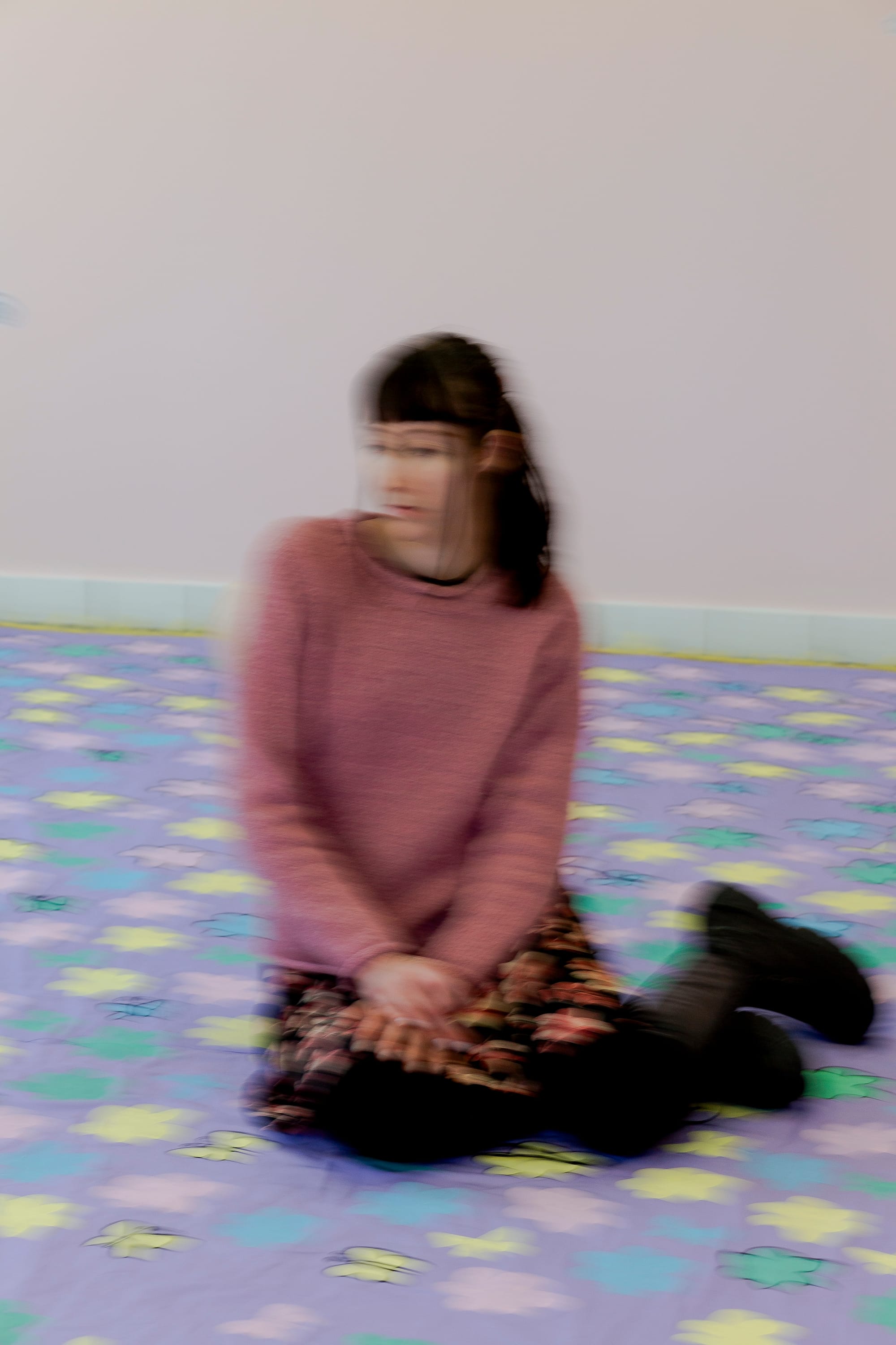 A blurred image of a woman wearing a pink sweater and floral skirt